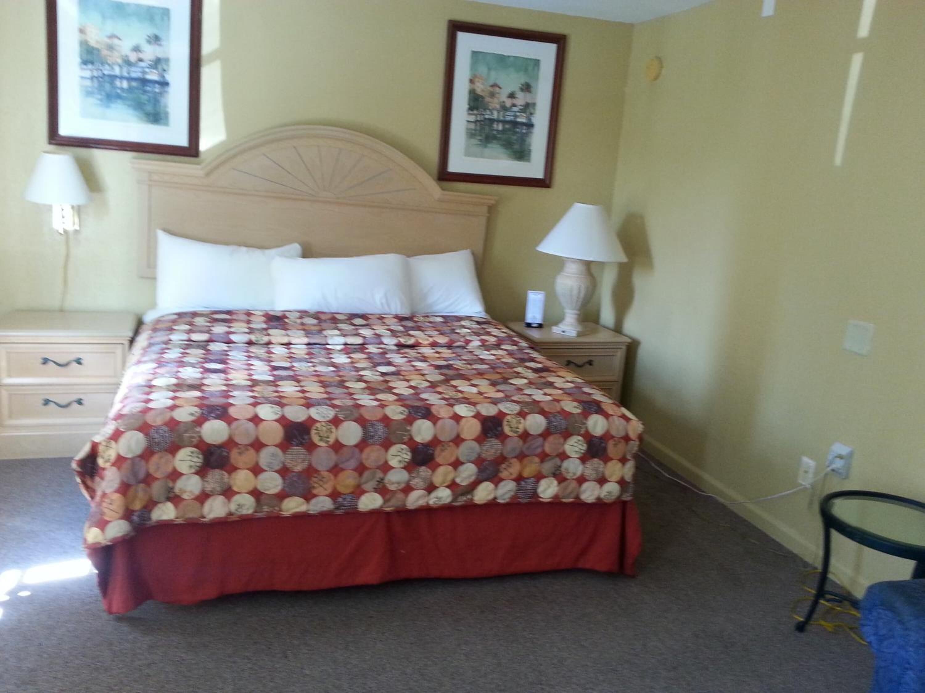 A neatly made bed with a patterned bedspread, two bedside tables with lamps, and two framed pictures on the wall.