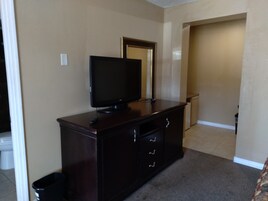 Una habitación con un aparador de madera oscura, un televisor de pantalla plana encima, un cubo de basura y una puerta que da a otra habitación.