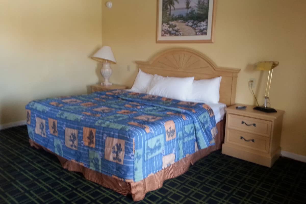 A hotel room with a large bed, a nightstand, a lamp, a drawer, and a framed picture on the wall.