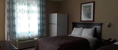 A hotel room with a bed, a desk, a chair, a wardrobe, and a window with curtains.