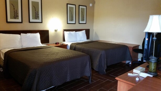 A hotel room with two beds, a nightstand, a lamp, and a desk with a phone and a coffee maker. - Budget Lodge of Mount Dora (Mount Dora)