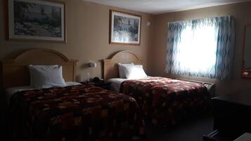 A hotel room with two beds, a nightstand, a lamp, and a window with curtains.