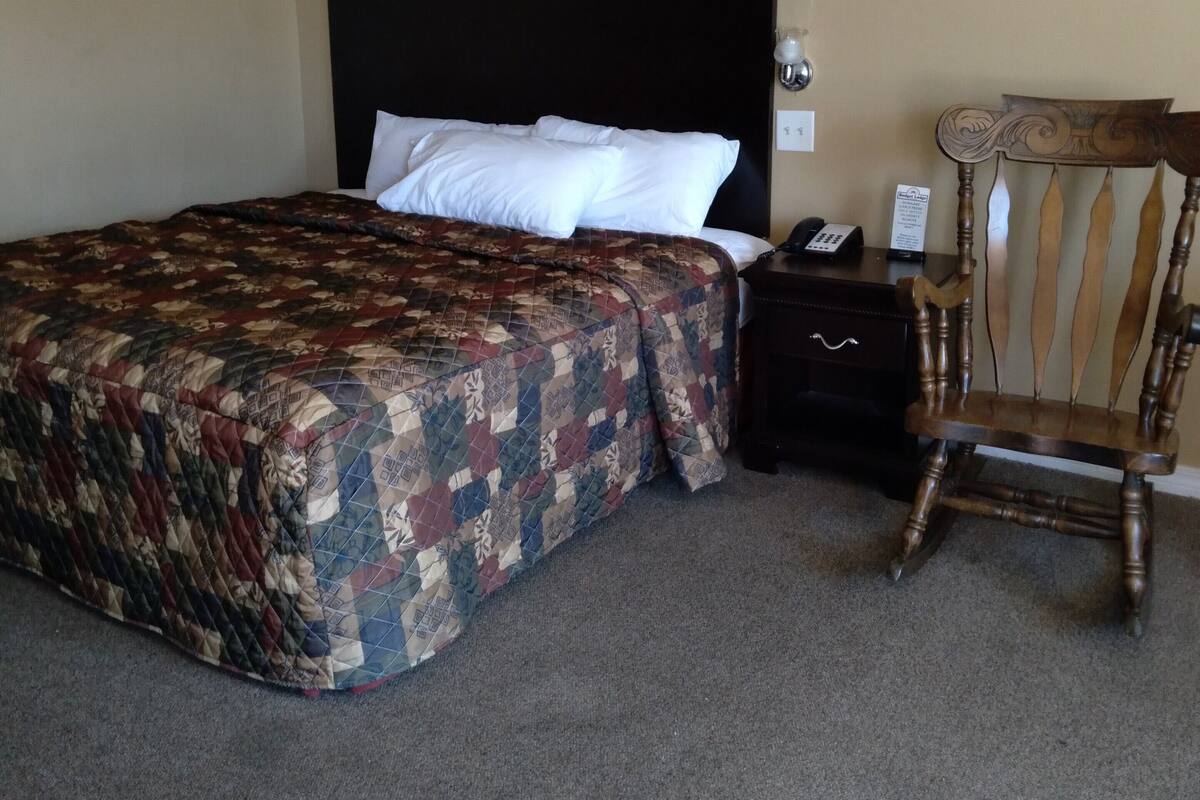 A hotel room with a large bed, a wooden chair, a nightstand, and a framed picture on the wall.