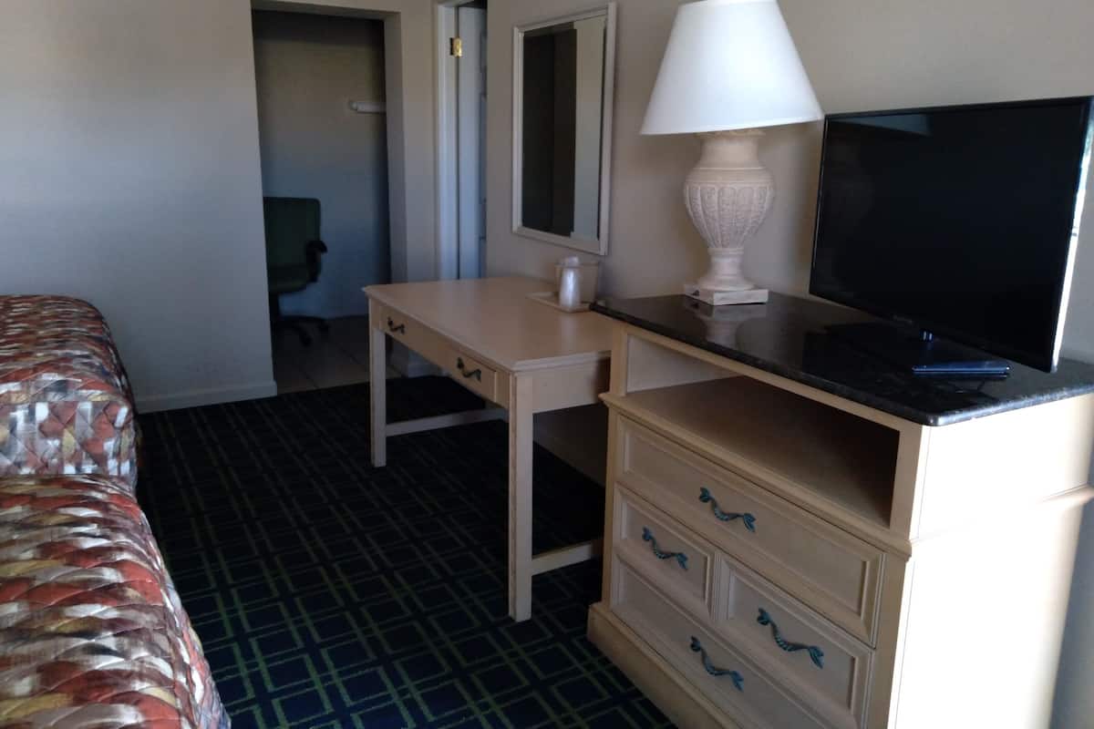A hotel room with a bed, a desk, a television, a lamp, and a chair.