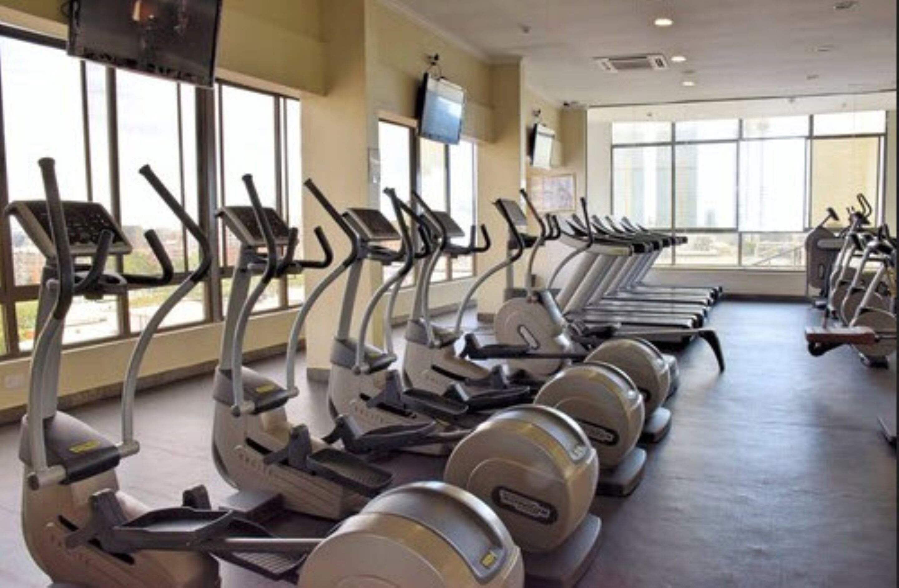 A gym with multiple treadmills and stationary bikes arranged in rows.