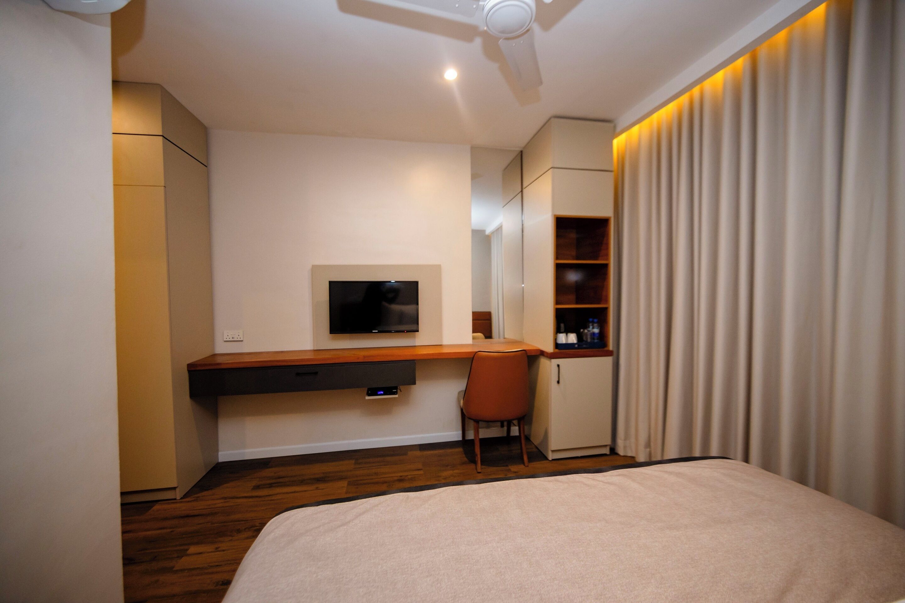 A hotel room with a bed, a desk, a television, a chair, and a wardrobe.