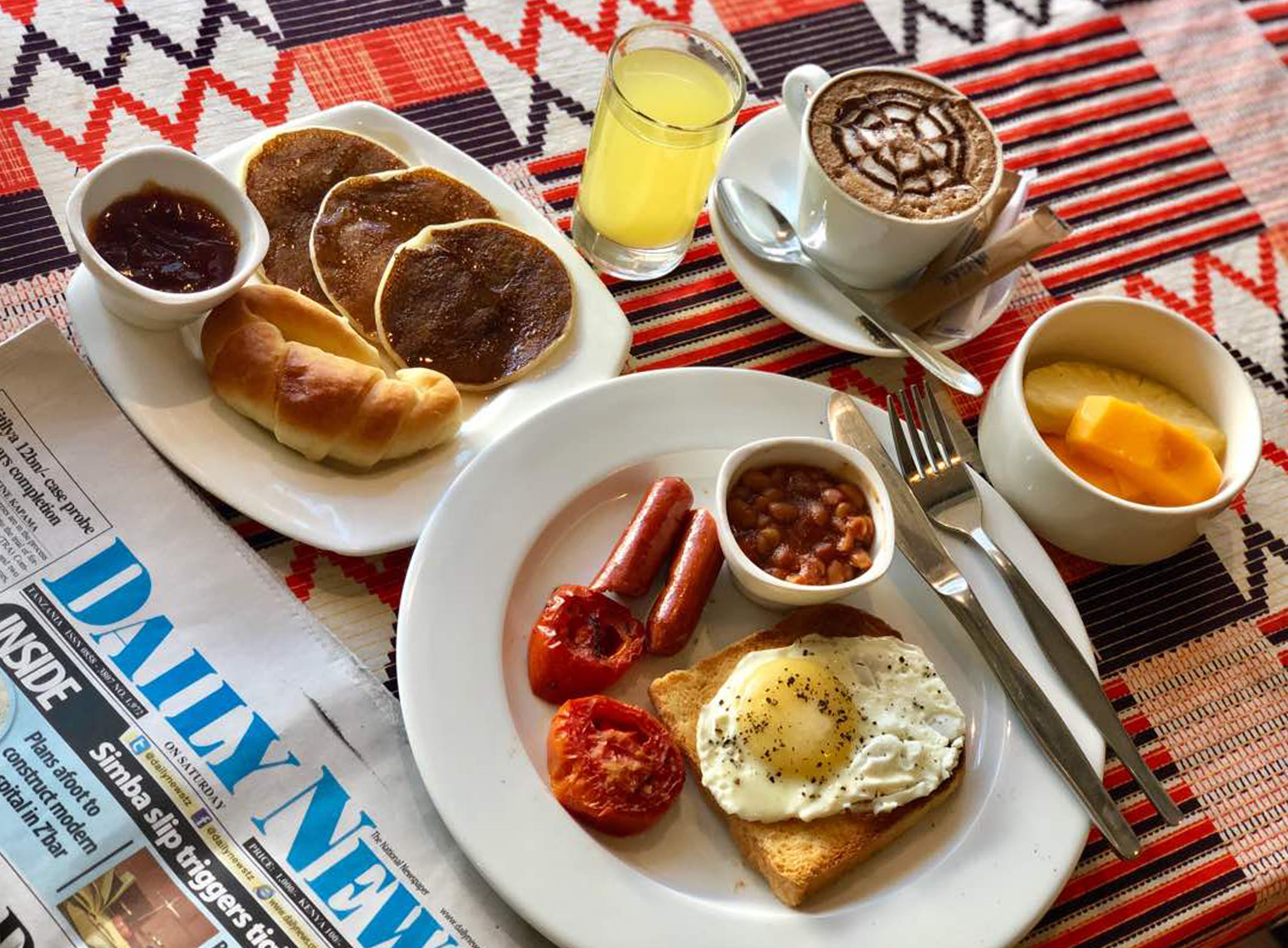 A breakfast plate with toast, eggs, beans, sausages, and a glass of orange juice.