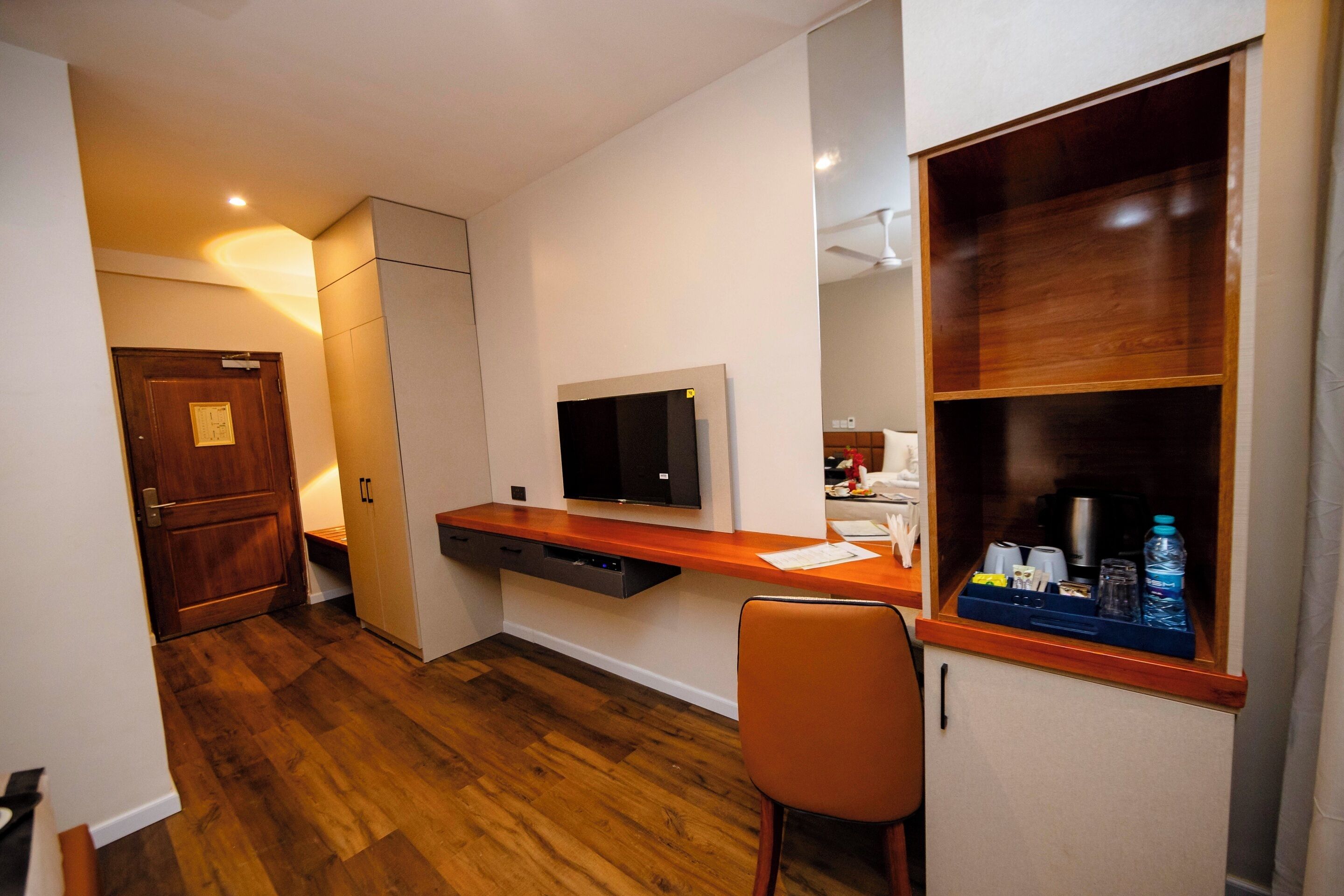 Ein Hotelzimmer mit Holzboden, einem Schreibtisch mit Flachbildfernseher, einem Sessel, einer Holzablage mit Pflegeprodukten und einer Tür.
