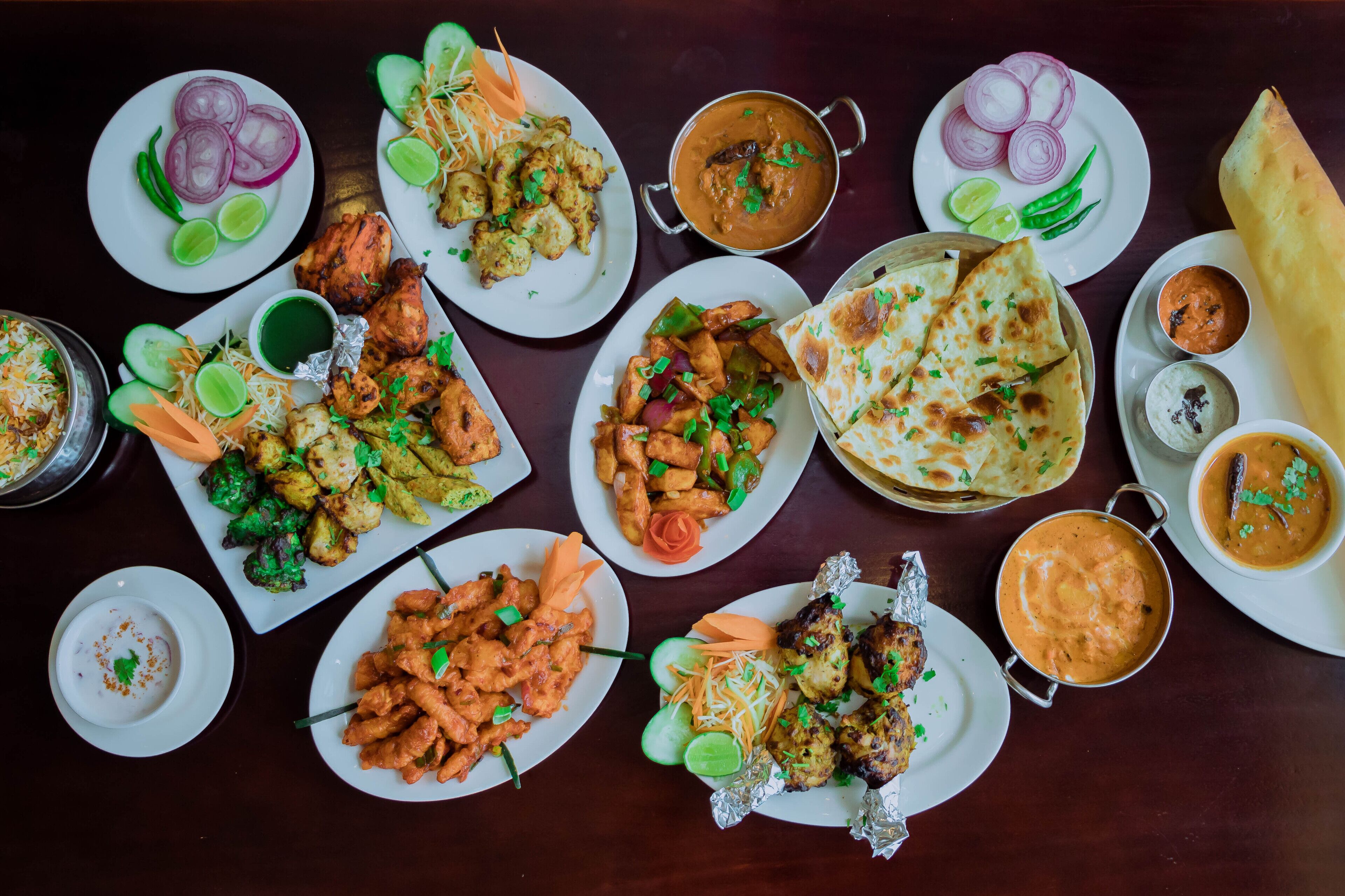 A variety of Indian dishes including naan bread, curries, and tandoori chicken, arranged on a table.