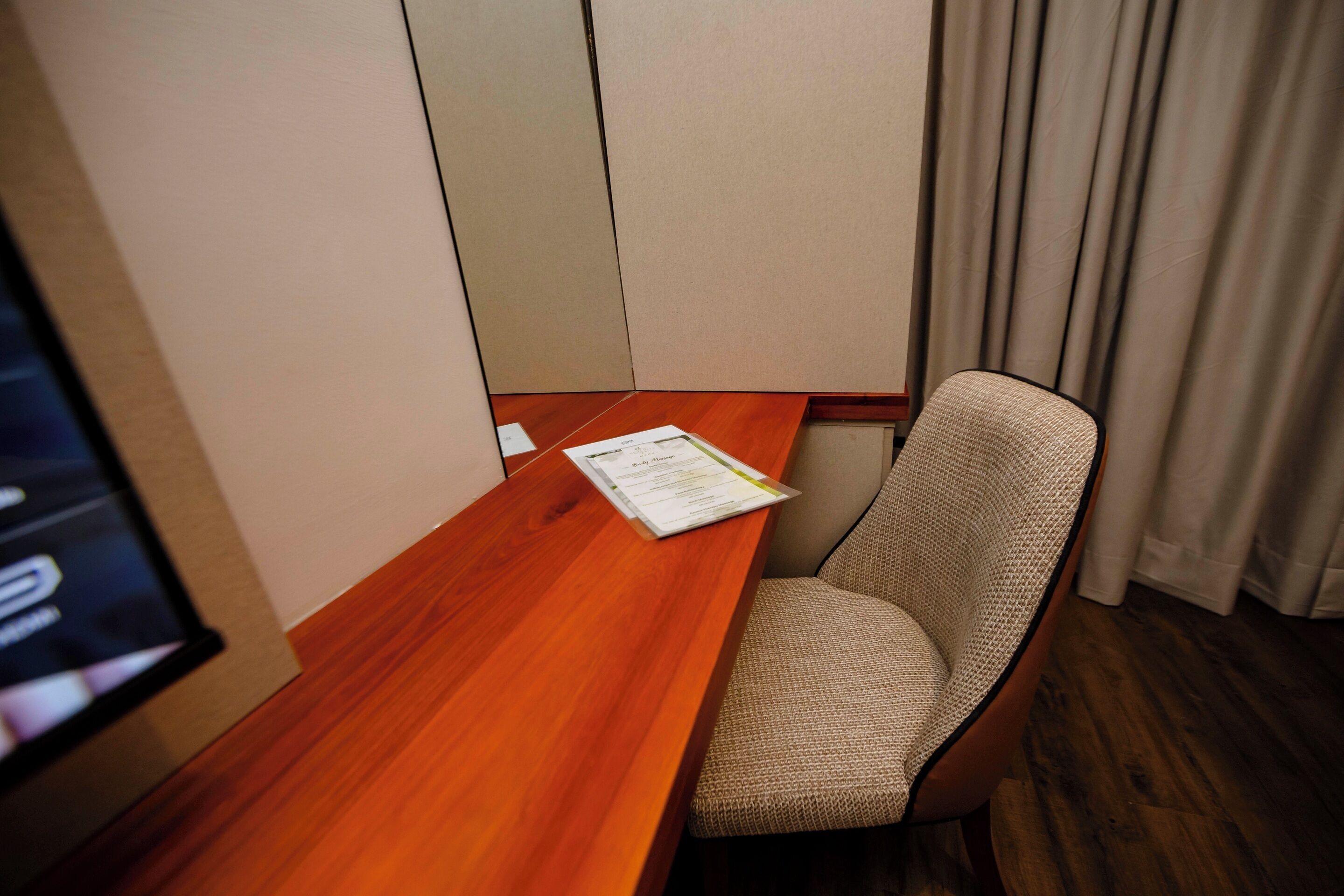 A hotel room with a wooden desk, a single chair, and a menu on the desk.