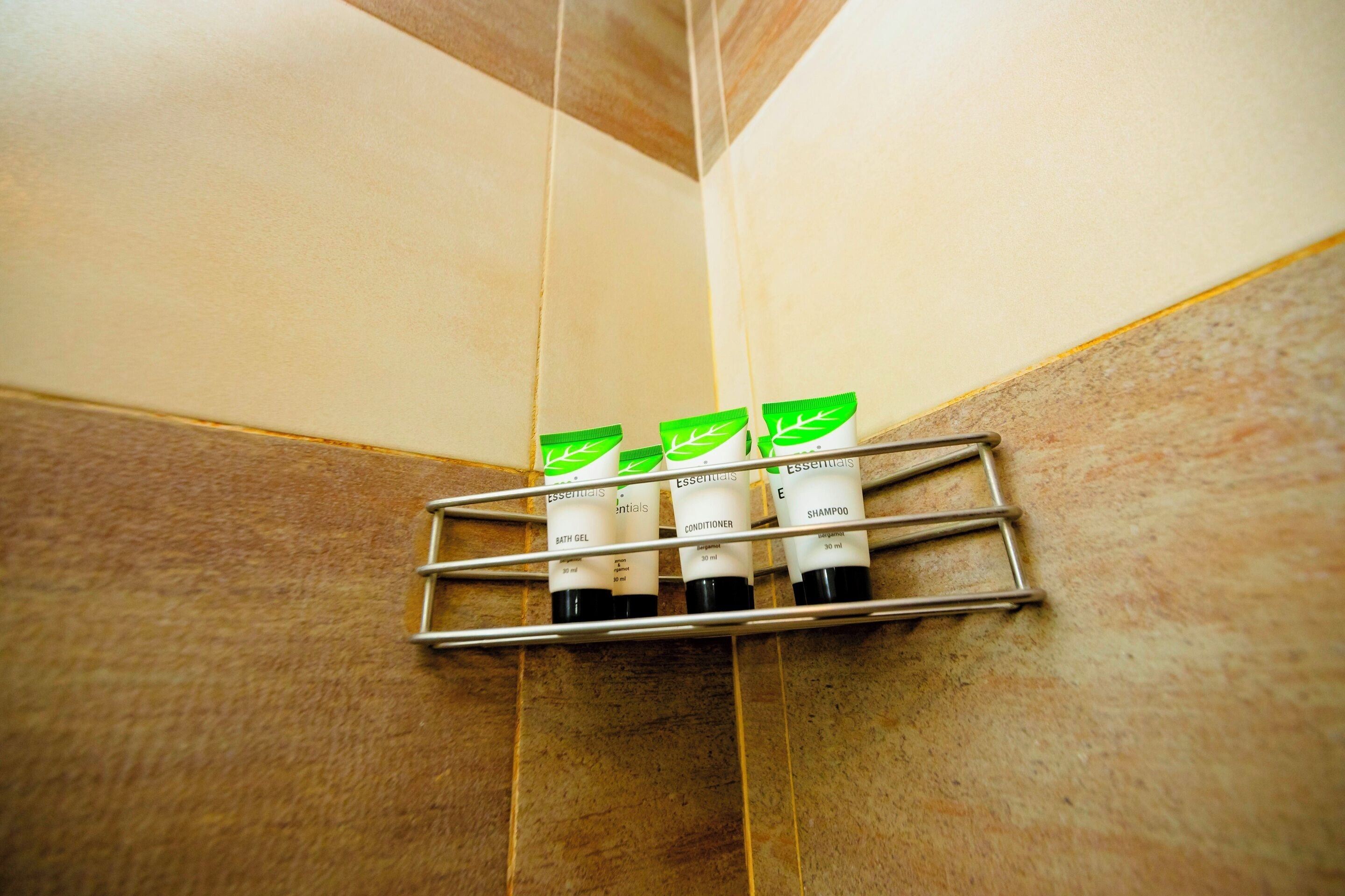 Rincón de baño con un estante que sostiene tres botellas de champú, acondicionador y gel de baño.