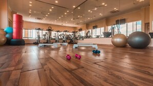 Un gimnasio amplio con suelo de madera, equipo de ejercicio y espejos grandes.