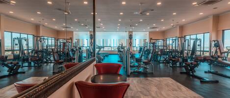A gym with mirrored walls, exercise equipment, and large windows.