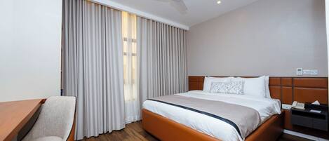 A hotel room with a bed, a desk, a chair, a ceiling fan, and a window with curtains.