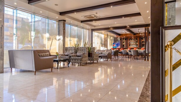 Un vestíbulo espacioso con un diseño moderno, que incluye una zona de estar con sofás y sillones estampados, un bar con una variedad de botellas y grandes ventanales con vistas al exterior.