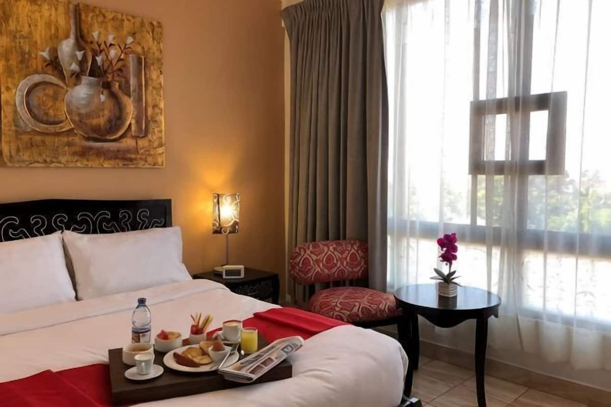 A hotel room with a bed, a bedside table with a tray of breakfast, a chair, and a window with curtains.