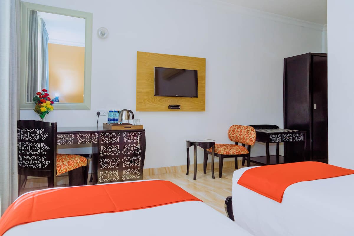 A hotel room with a bed, a desk with a chair, a television mounted on the wall, and a wardrobe.