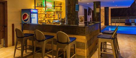 A bar area with a Pepsi refrigerator, bar stools, and a pool in the background.