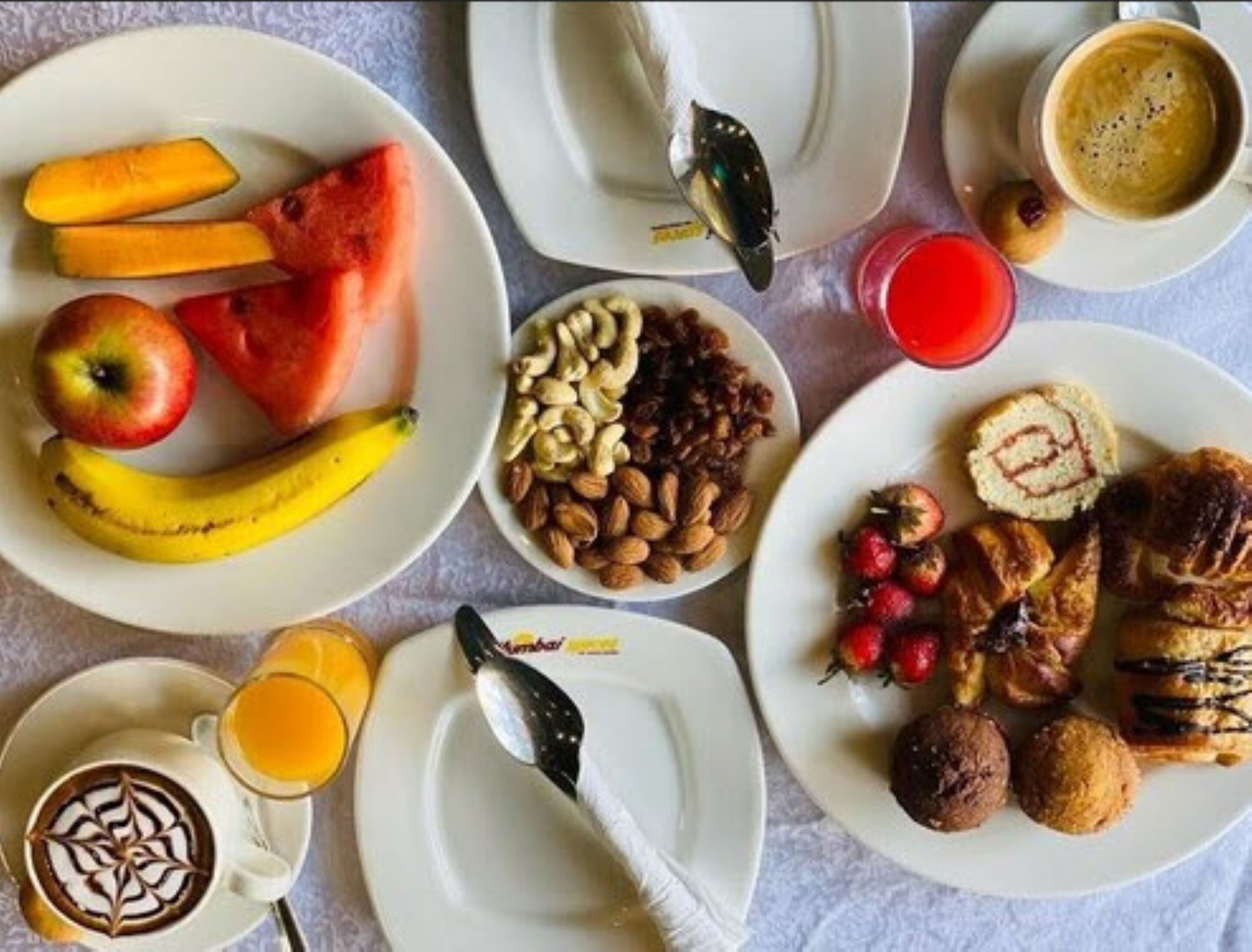 A breakfast spread with various fruits, nuts, pastries, and beverages on plates.
