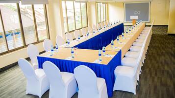 A conference room with a long table, white chairs, and a projector screen.
