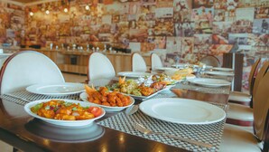 Una mesa de comedor lista para una comida, con diferentes platos, sillas blancas y una pared decorada con fotografías.