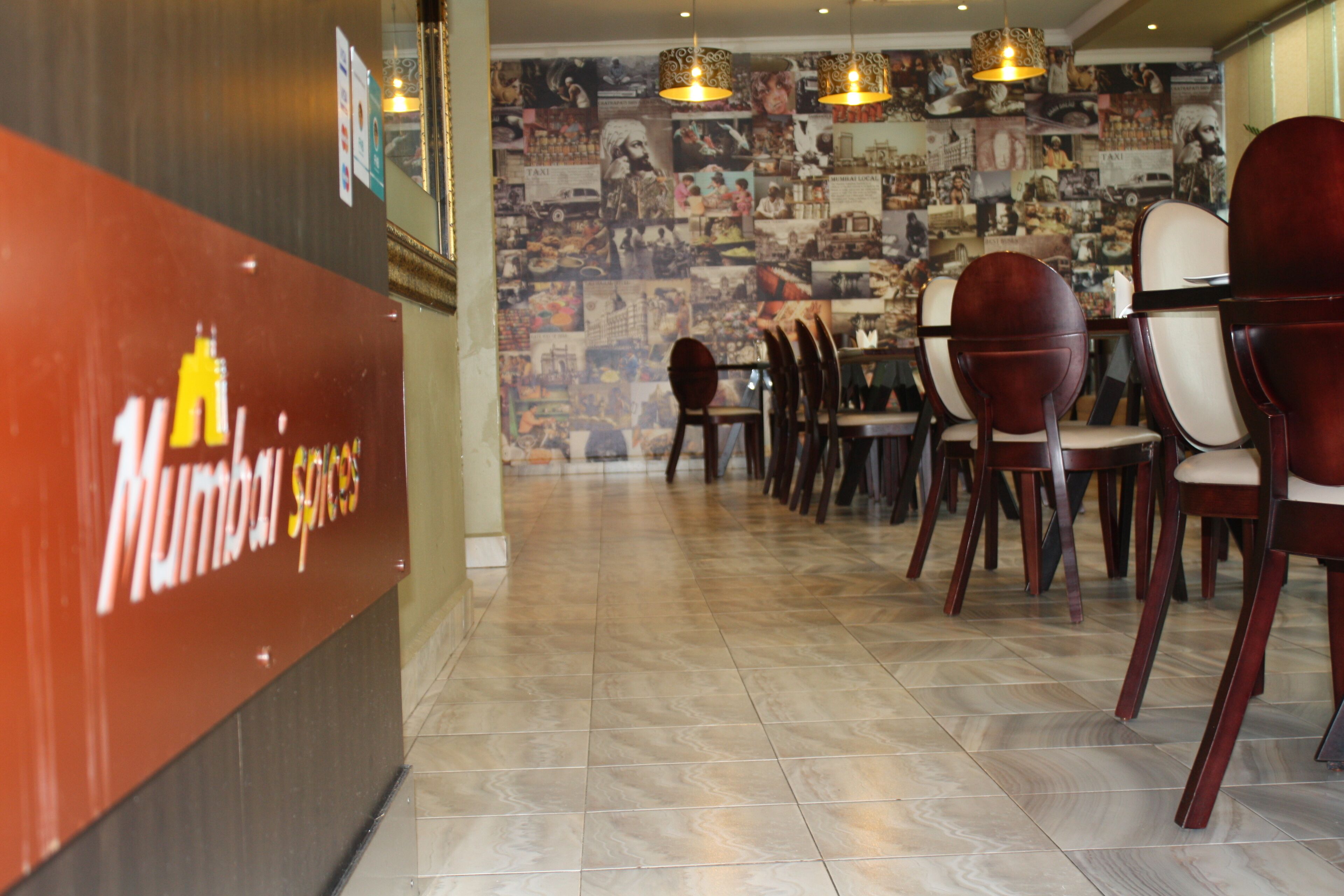 A restaurant interior with a wall of photographs, wooden chairs, and a sign reading "Mumbai Spices".