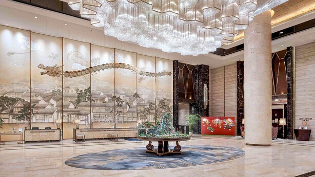 A lobby with a large chandelier, a reception desk, a decorative wall with traditional artwork, and a central fountain. - Pullman Weifang (Weifang)