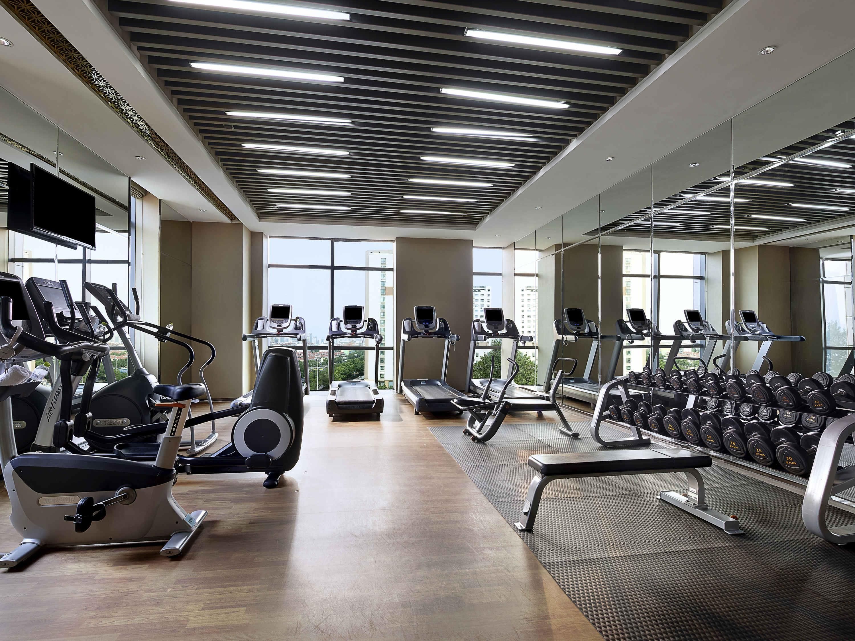 Une salle de sport équipée de tapis de course, de vélos elliptiques et d’un mur recouvert de miroirs.