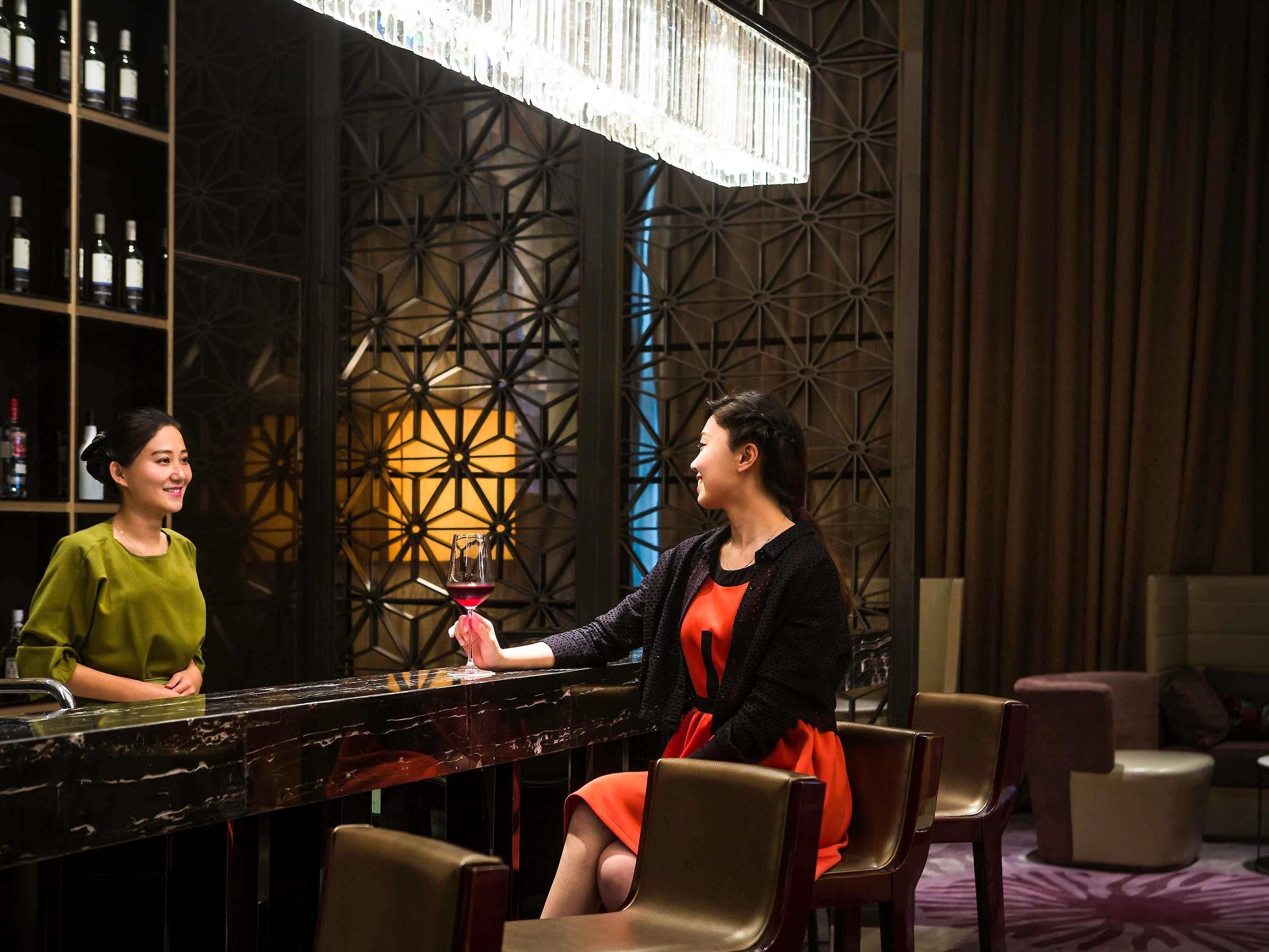 A bar area with a patterned wall, a chandelier, and a bar counter.