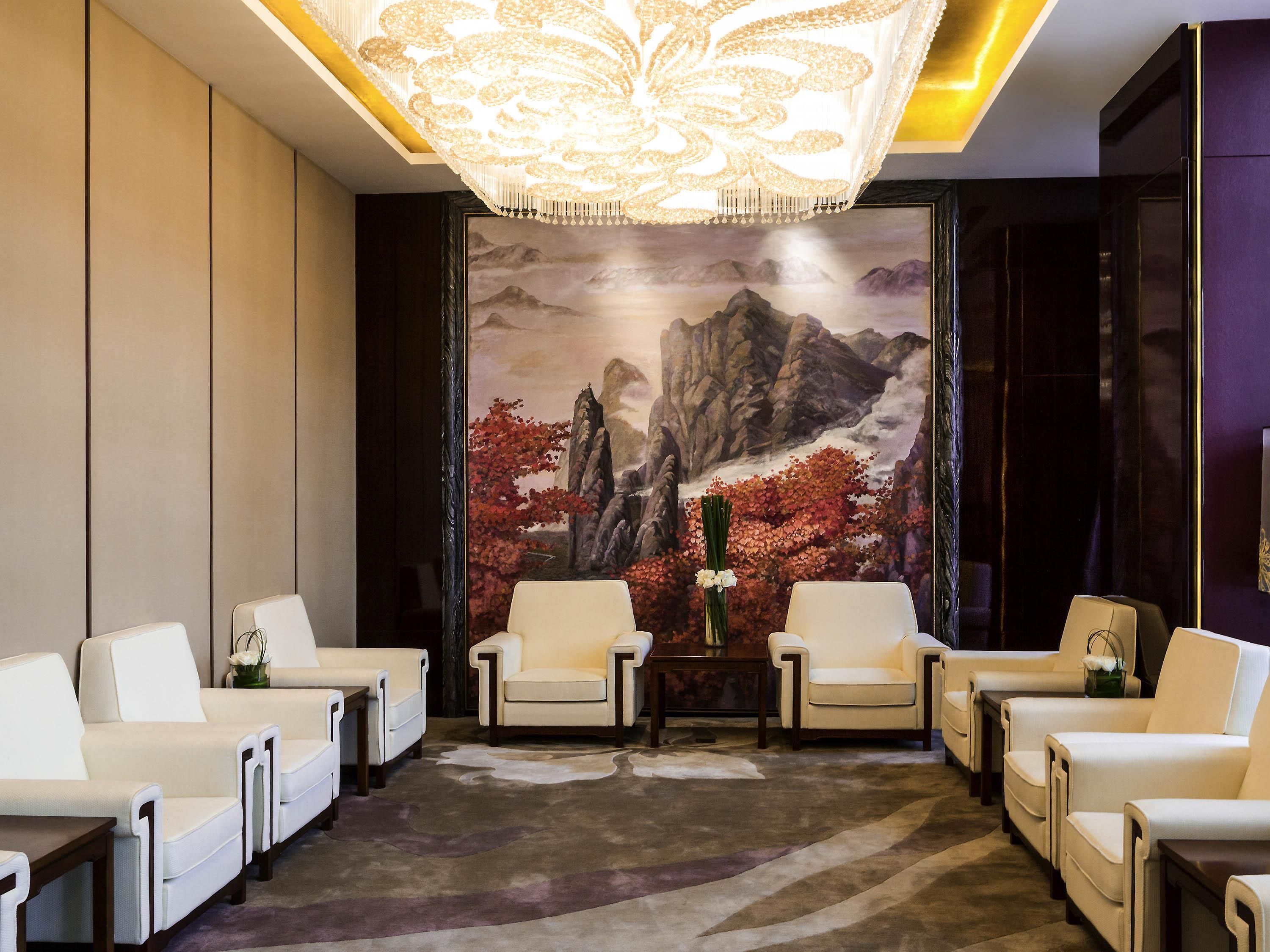 A lobby with a large mural, multiple seating areas, and a chandelier.