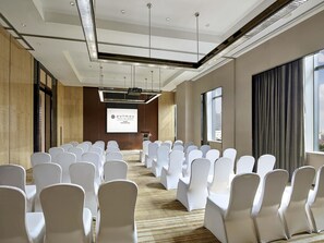 A conference room with rows of white chairs, a projector screen, and a large window. - Pullman Weifang (Weifang)