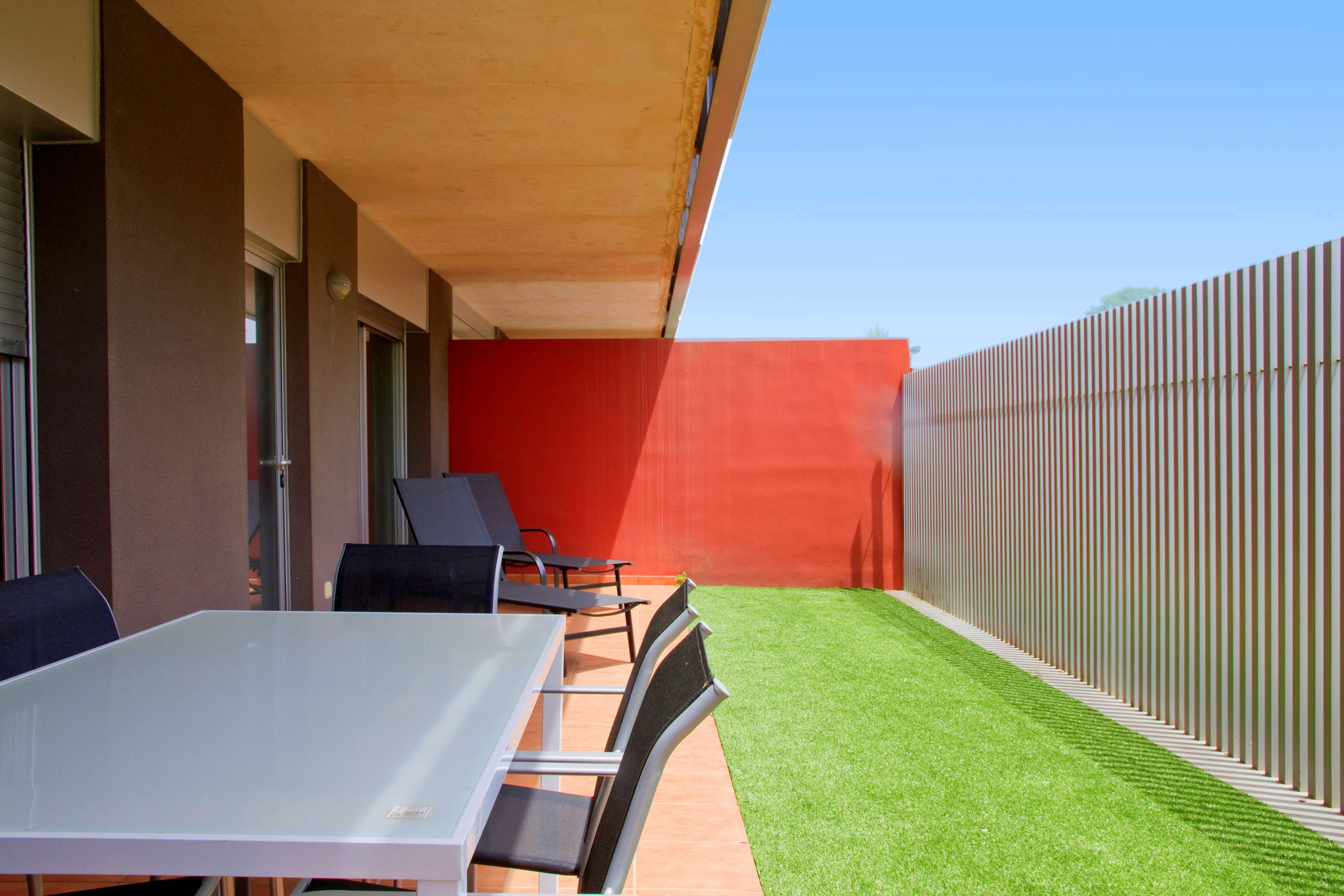 A patio with a table and chairs, a red wall, and a fence.