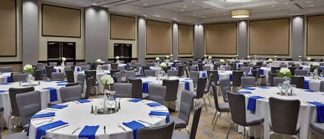 Un salón de conferencias amplio con mesas redondas, sillas grises y manteles azules.