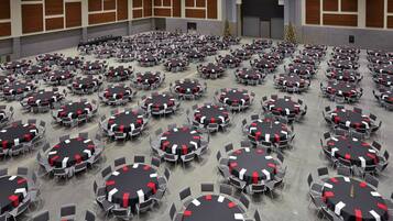 A large conference room with multiple round tables, each with a black tablecloth and red and white sashes.