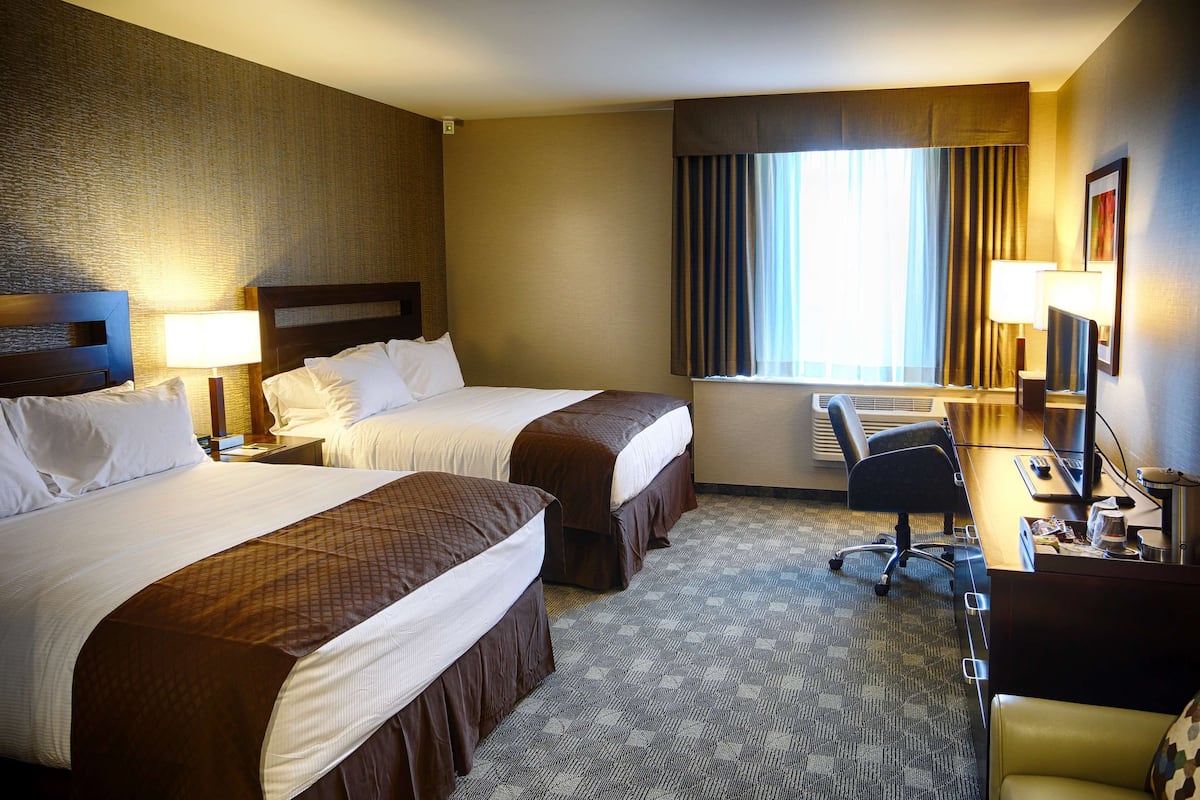 A hotel room with two beds, a desk, a chair, a lamp, and a window with curtains.