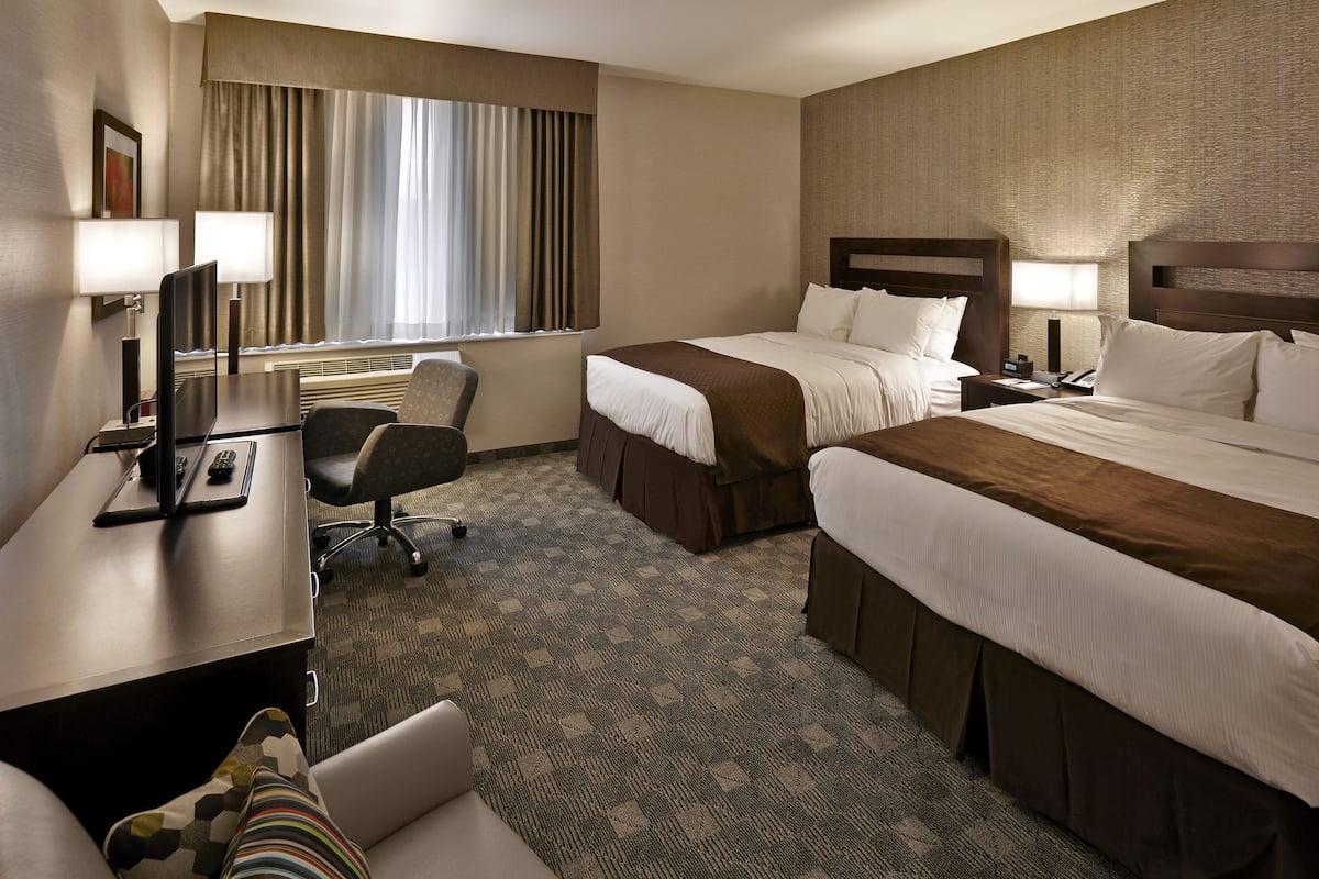 A hotel room with two beds, a desk with a computer, a chair, and a window with curtains.