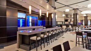 Una hall moderna di un hotel con area bar, posti a sedere e un grande schermo che mostra contenuti.
