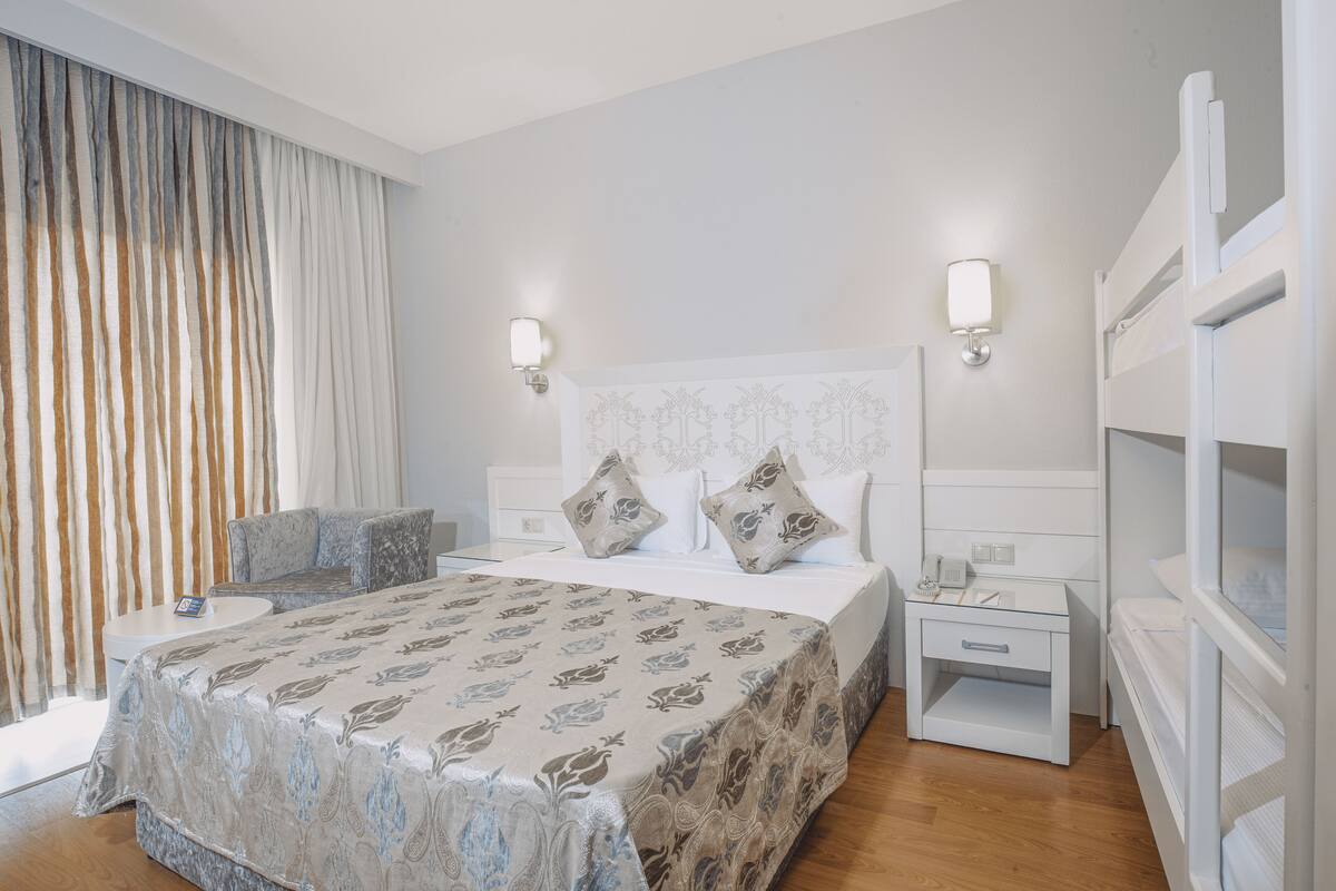 Een hotelkamer met een groot bed, twee nachtkastjes, een zithoek en een stapelbed.