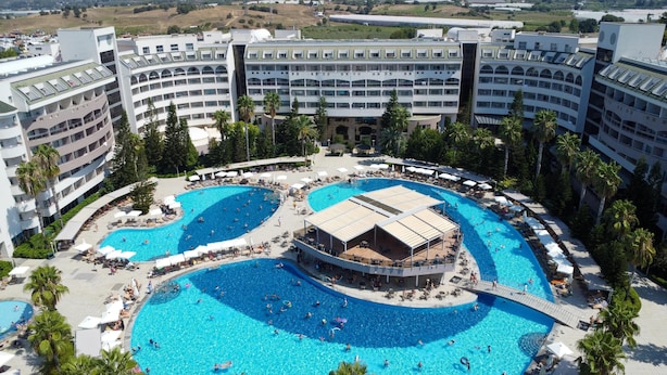 A large hotel with multiple swimming pools, a central covered area, and a surrounding landscaped area with palm trees. - Amelia Beach Resort Hotel & Spa (Manavgat)
