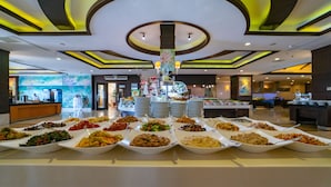 A buffet with various dishes arranged in white bowls, a modern ceiling design with circular patterns, and a reception area in the background. - Amelia Beach Resort Hotel & Spa (Manavgat)