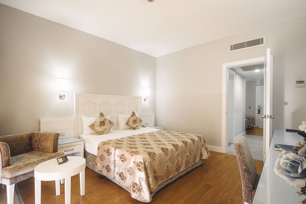 Een hotelkamer met een bed, een bank, een klein tafeltje en een stoel. Er is een deur die naar een andere kamer leidt.