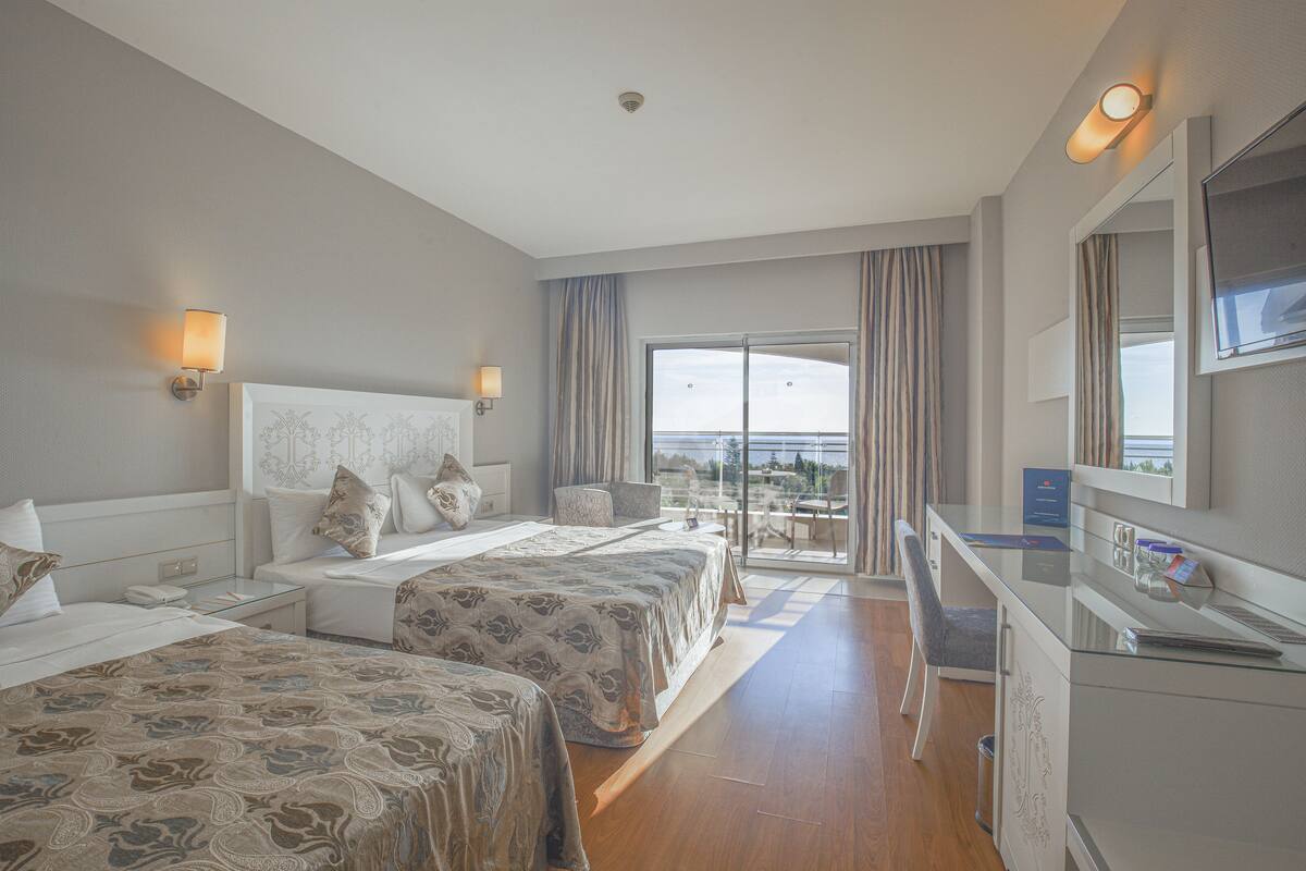 Een hotelkamer met twee bedden, een bureau, een televisie en een balkon met gordijnen.