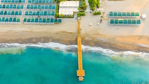 An aerial view of a beach resort with a wooden pier leading to a row of beachside rooms. - Amelia Beach Resort Hotel & Spa (Manavgat)