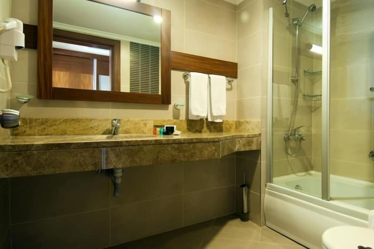 Une salle de bain dotée d’un comptoir en marbre, d’un lavabo, d’un miroir, de toilettes et d’une douche à parois de verre.