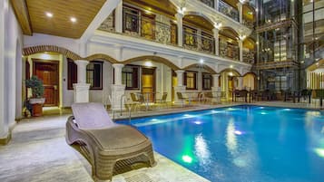 An indoor swimming pool with a lounge chair, multiple balconies, and ornate architectural details.
