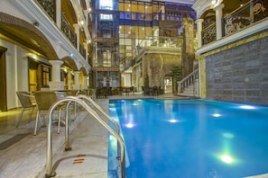 Una piscina interior con techo de cristal, paredes de piedra y una escalera que lleva a niveles superiores.