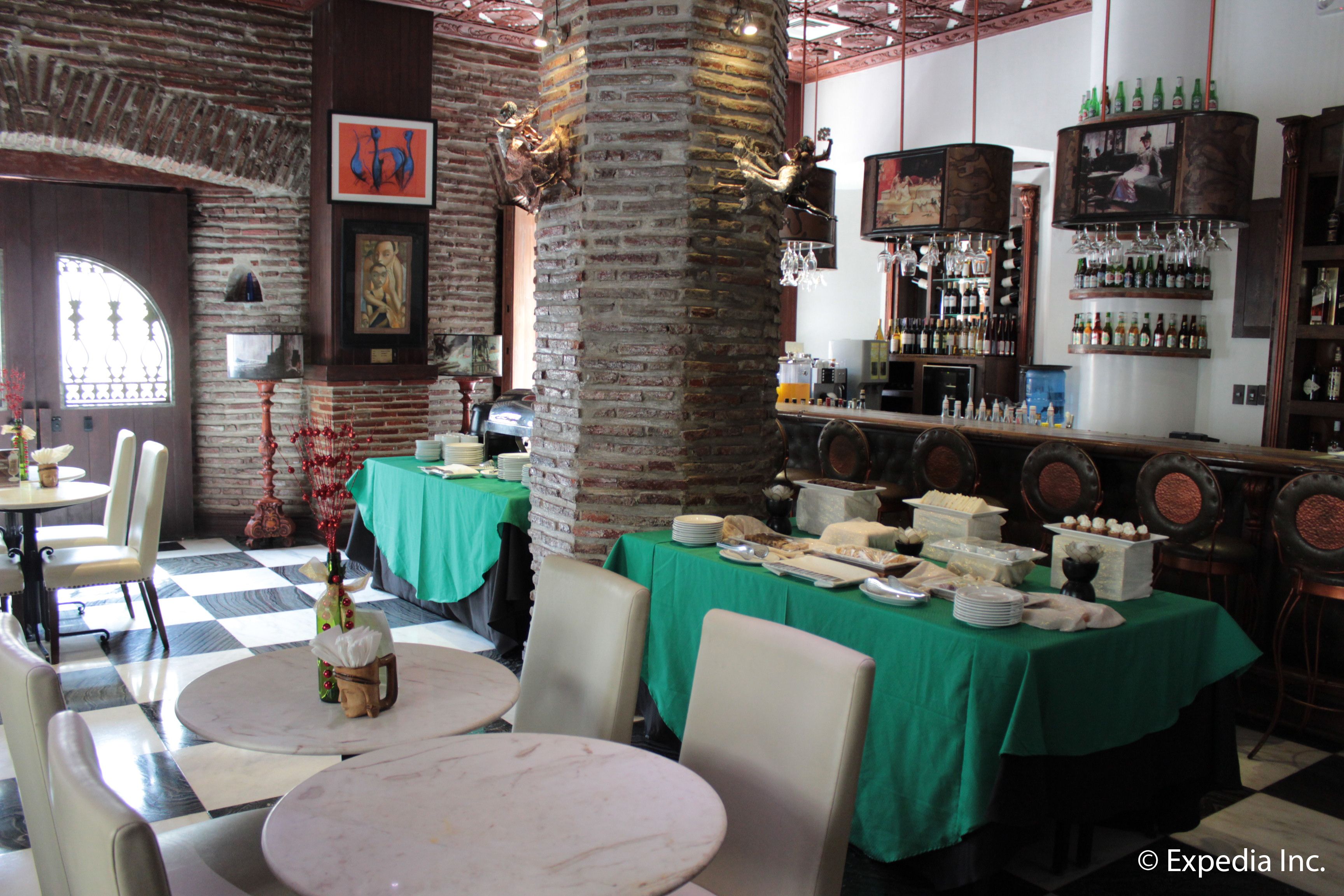 A restaurant with brick walls, green tablecloths, and a bar area with bottles and glasses.