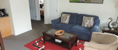 A living room with a blue sofa, a glass coffee table, a red rug, and a beige armchair.