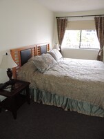 Un dormitorio con una cama grande, una mesita de noche con lámpara y una ventana con cortinas.