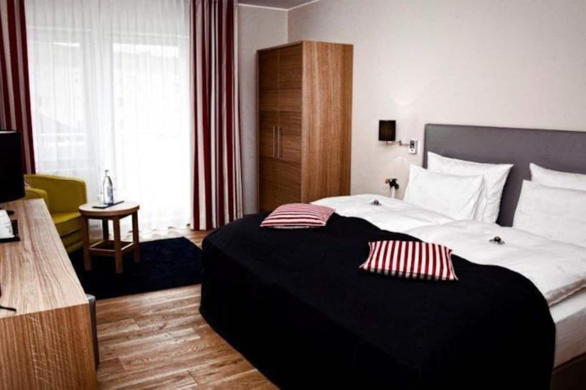 Een hotelkamer met een bed, een houten garderobe, een bureau en een stoel.